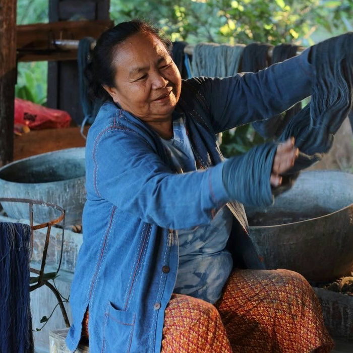 A dyer lifting a hank of yarn from a natural indigo vat